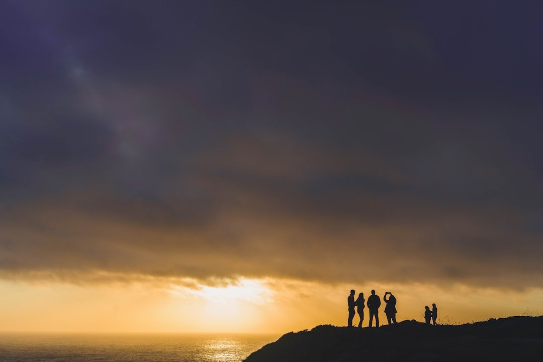 six people standing on mountain cliff at golden hour