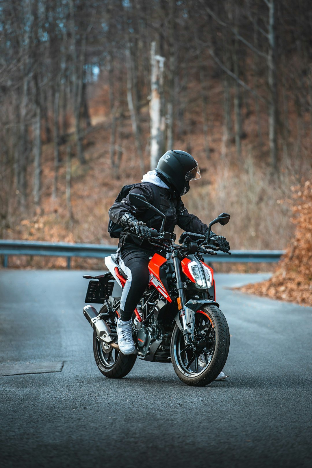 man in black jacket riding orange and black motorcycle on road during daytime