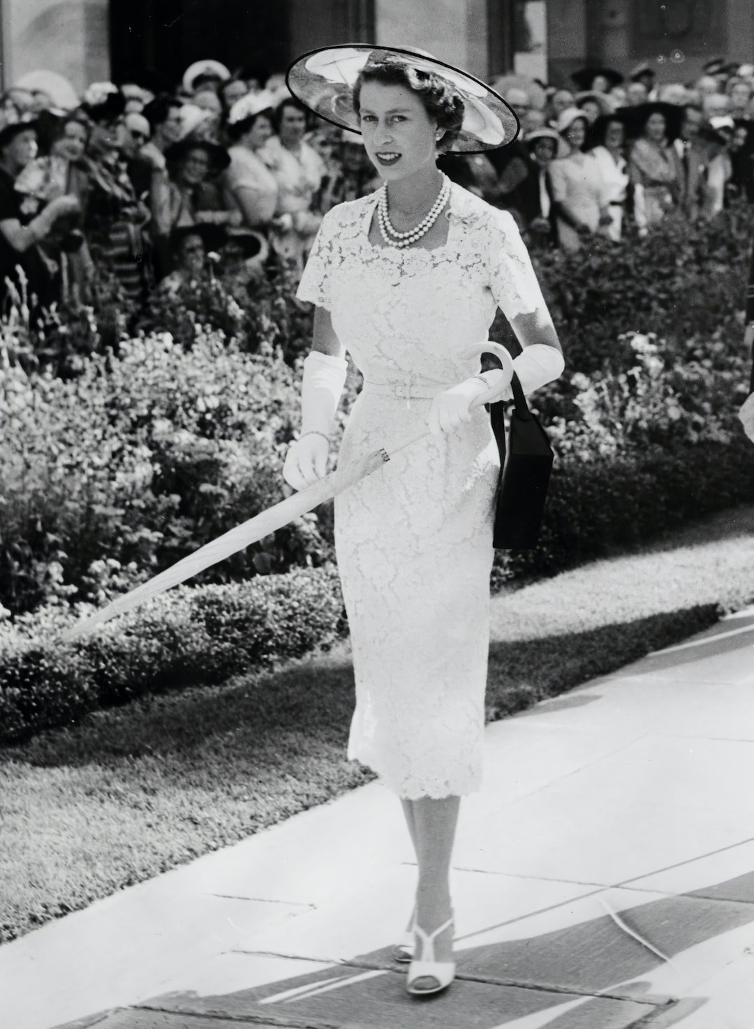 a woman in a white dress and hat walking down a sidewalk