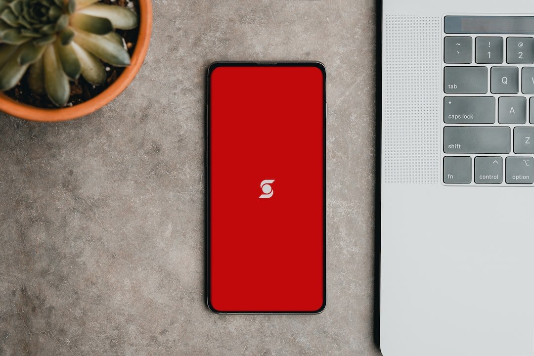 a red cell phone sitting next to a laptop computer